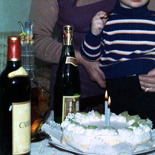 Woman holds baby, celebrating with cake and drinks.