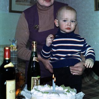 Woman holds baby, celebrating with cake and drinks.