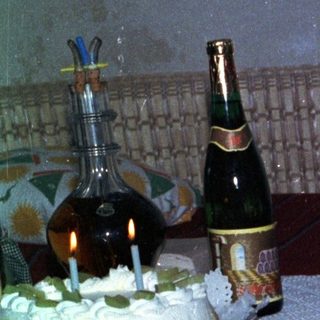 Baby sits near a table with cake and drinks.