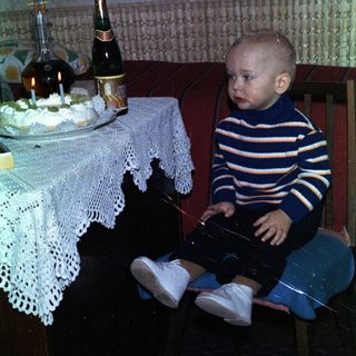 Baby sits near a table with cake and drinks.