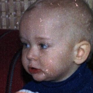 Baby sits near a table with cake and drinks.