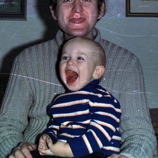 Man holds baby with wine and artwork in background.