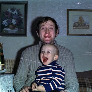 Man holds baby with wine and artwork in background.