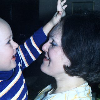 Baby playfully touches a woman's nose in a close-up.