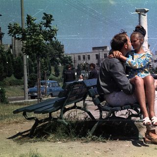 Couple sits on a park bench in a vintage scene.