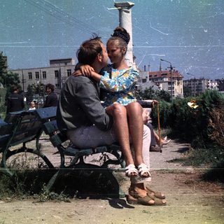 Couple sits on a park bench in a vintage scene.