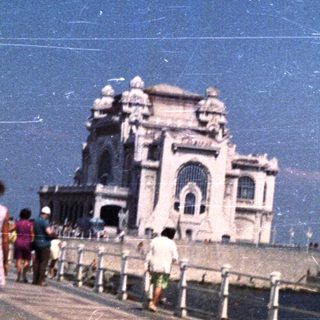 People walk along a promenade with a building in the background.