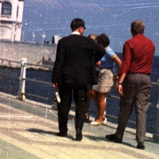 People walk along a promenade with a building in the background.