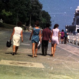 People walk along a promenade with a building in the background.
