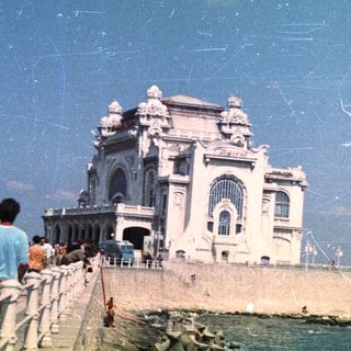 People stroll along a coastal promenade with a grand building.
