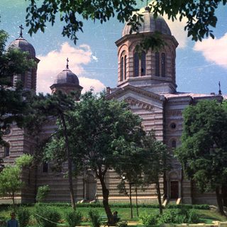 Grand church building stands amidst trees and greenery.