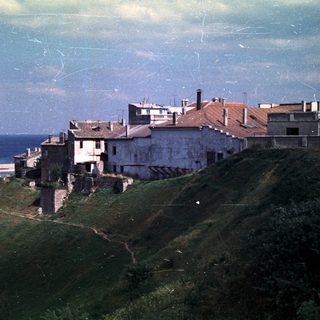 Buildings cling to a hillside overlooking a beach and sea.
