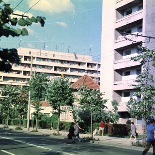 Apartment building with people on a street, trees visible.