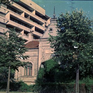 Building facade and small structure with trees in foreground.