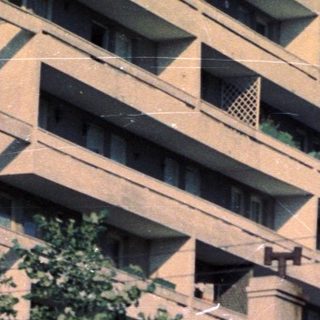 Building facade and small structure with trees in foreground.