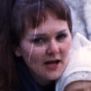 Woman with baby in stroller stands in grassy area.