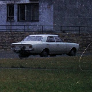 Concrete apartment building with people and a car.