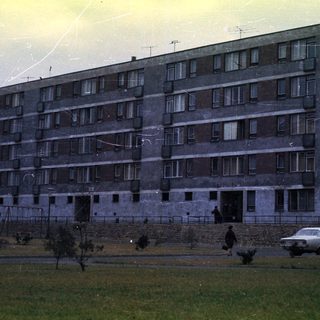 Concrete apartment building with people and a car.