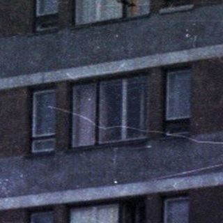 Concrete apartment building with people and a car.