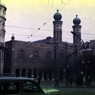 Synagogue with surrounding buildings and people on a street.
