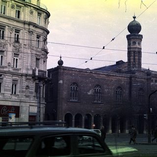 Synagogue with surrounding buildings and people on a street.