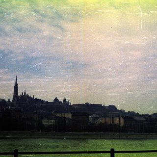 City skyline over water, likely Budapest, with a church spire.