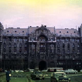 Grand, ornate building with vintage cars and pedestrians nearby.