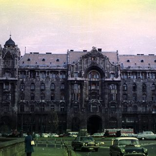 Grand, ornate building with vintage cars and pedestrians nearby.