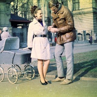 Couple stands near a pram on a city street.