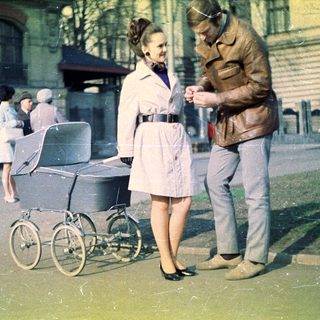 Couple stands near a pram on a city street.