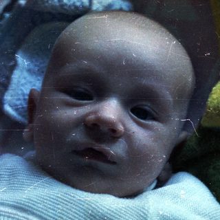 Baby lying wrapped in a blanket, looking at the camera.
