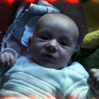Baby lying wrapped in a blanket, looking at the camera.