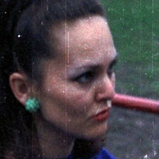 Woman sits on a bench, wearing a blue sweater and skirt.