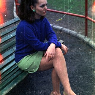 Woman sits on a bench, wearing a blue sweater and skirt.