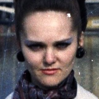 Woman in trench coat stands on bridge, looking down.
