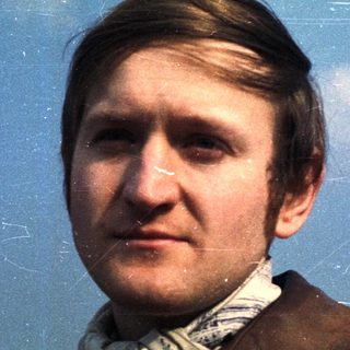 Man in a brown jacket against a cloudy sky.