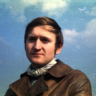 Man in a brown jacket against a cloudy sky.
