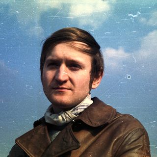 Man in a brown jacket against a cloudy sky.