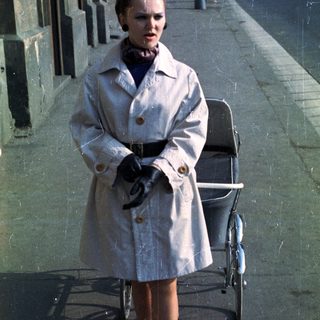 Woman in coat stands next to a vintage pram.