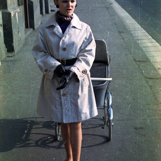 Woman in coat stands next to a vintage pram.