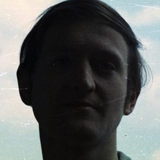 Man looking at the camera outdoors on a cloudy day.