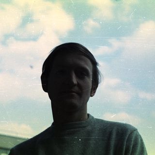 Man looking at the camera outdoors on a cloudy day.