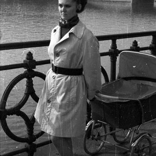 Woman stands near a pram with a river in background.