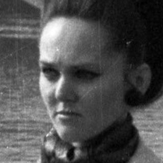Woman stands near a pram with a river in background.