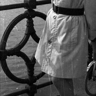 Woman stands near a pram with a river in background.