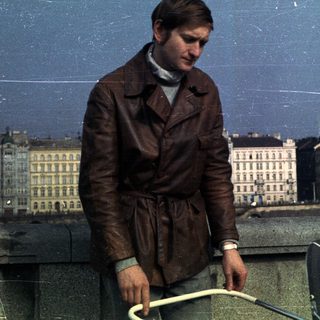 Man in a leather coat overlooks a city skyline.