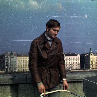 Man in a leather coat overlooks a city skyline.