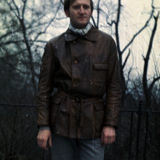 Man stands outdoors in a leather jacket and jeans.