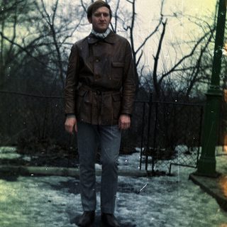Man stands outdoors in a leather jacket and jeans.