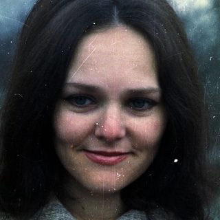 Here's a brief summary of the image: Woman with dark hair and blue eyes wearing a sweater.